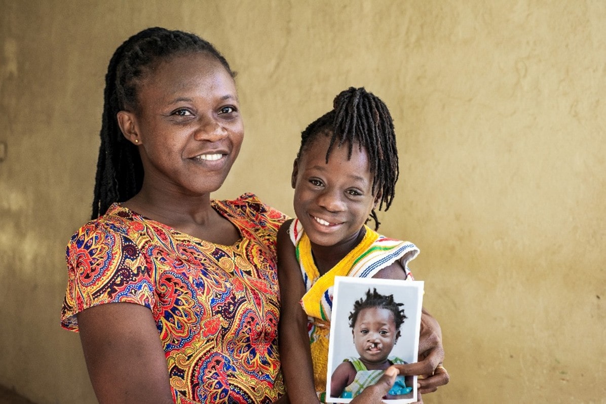 An adult holding a child and a printed photo against a plain wall background.