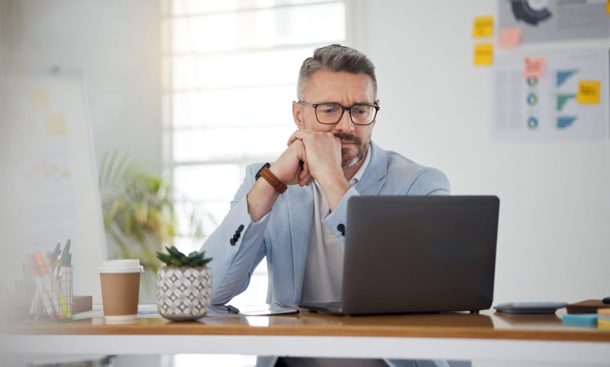 Person sitting at a desk with a laptop, coffee cup, and office supplies in a bright workspace.