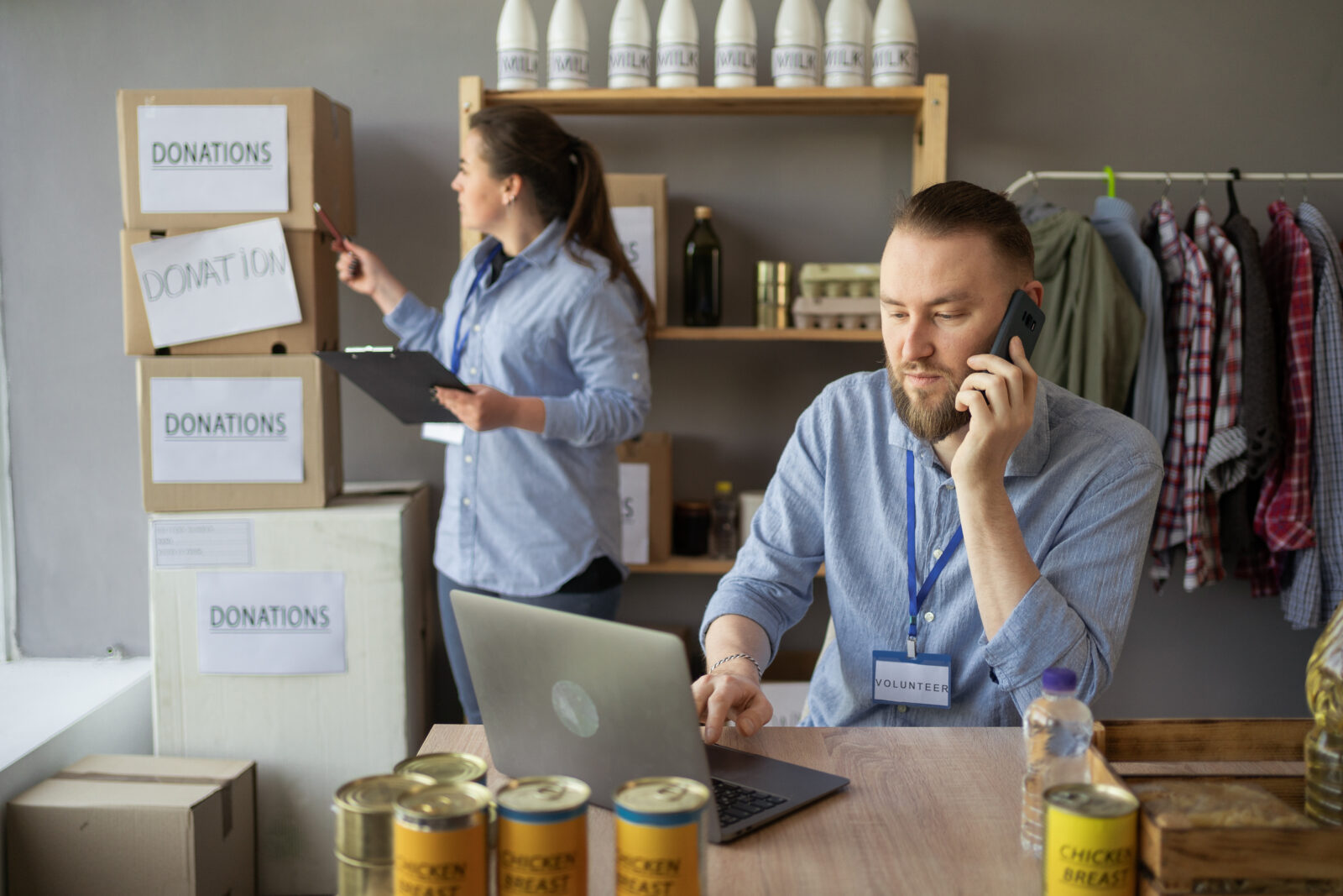 Charity, donation and volunteering concept. Male volunteer working use laptop and call on smartphone at distribution or refugee assistance center.