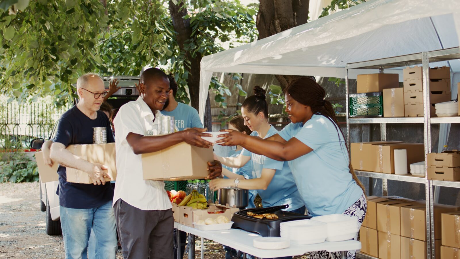 Needy individuals are provided with meal boxes and canned goods by dedicated volunteers. Smiling charity workers representing the food drive and nonprofit organization feed the homeless people.