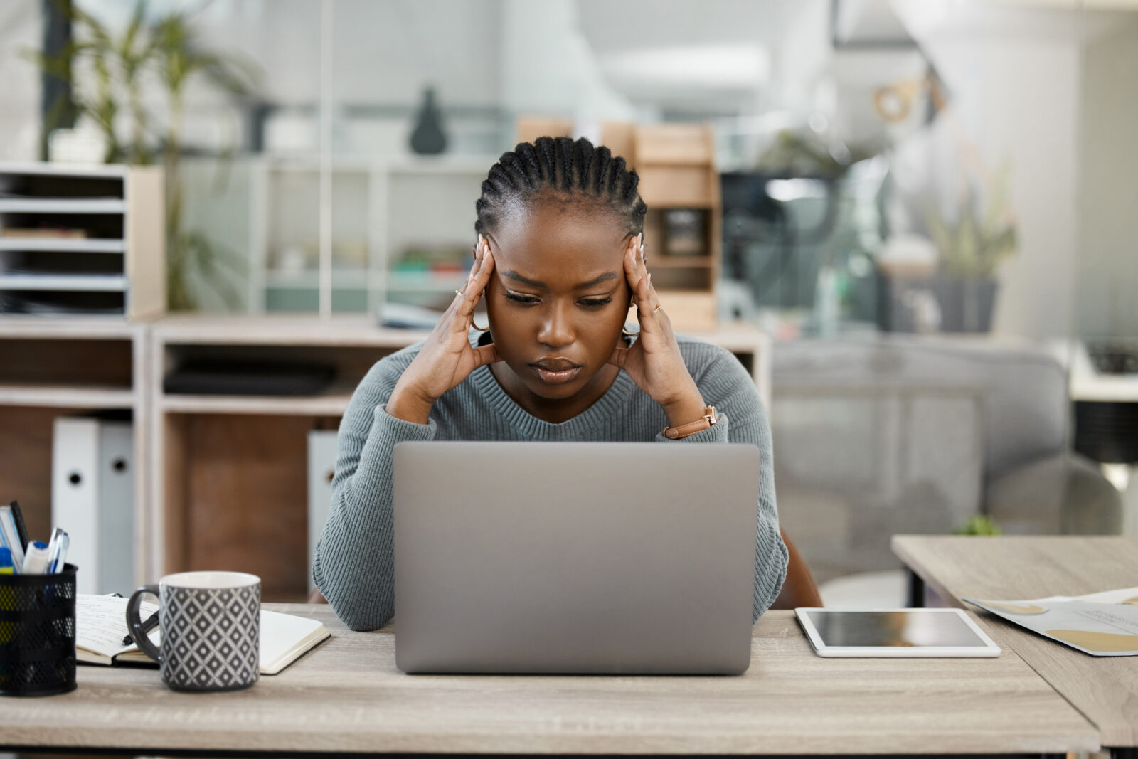 Woman at workplace in front of her computer stressed out holding the sides of her head with both hands.